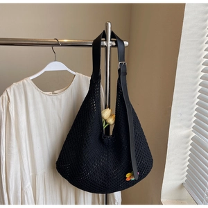 Detail of black crochet tote bag featuring leather strap and colorful flower charm