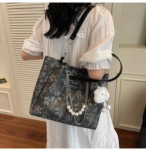 Detail of grey floral tote bag with silver chain, pearl charm and plush cloud accessory