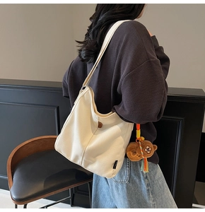 Détail du sac seau en toile blanche avec bandoulière large et breloque ours brun
