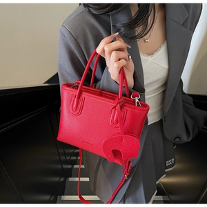 Detail of red lychee texture tote bag with elephant charm and silver metal hardware accents