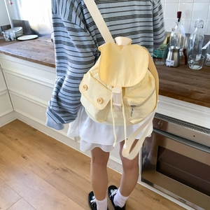 Light yellow nylon drawstring backpack with multi-pocket design shown in lifestyle scene