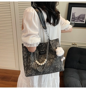 Detail of grey floral canvas tote bag with pearl chain strap and plush pendant decor