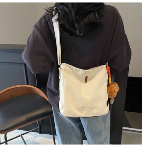 Vue détaillée du sac seau en toile blanche avec bandoulière large et charme d'ours brun