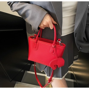 Detail of red lychee pattern leather handbag featuring a cute elephant charm accessory