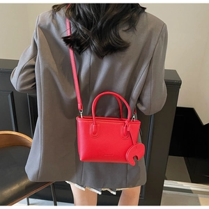 Red lychee texture leather bag shown on model with shoulder strap and charm