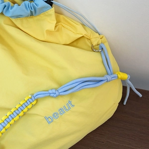 Detail of nylon crossbody bag featuring blue beaut embroidery and yellow drawstring