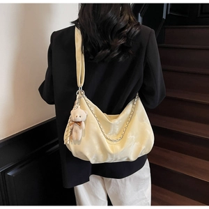 Close-up of a cream hobo bag with silver chain and teddy charm on a model's shoulder