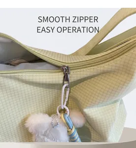 Close-up of smooth metal zipper and plush bear charm on green plaid canvas bag