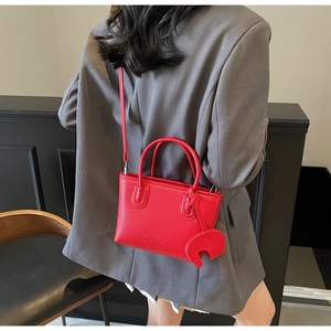Detail of red litchi texture handbag with elephant charm on model's shoulder