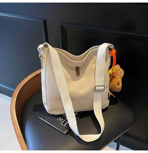 Détail du sac seau en toile crème avec étiquette en cuir et breloque ourson