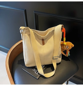 Détail du sac seau en toile beige avec étiquette en cuir et porte-clé ours en peluche