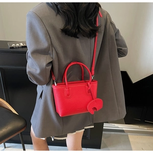Detail of red lychee pattern tote bag with elephant charm worn over a grey blazer