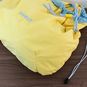 Detail of waterproof nylon crossbody bag featuring yellow body with blue beaut embroidery