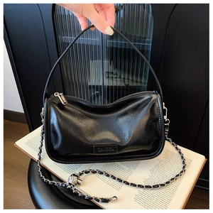 Detail of black patent leather handbag with silver chain strap and brand logo