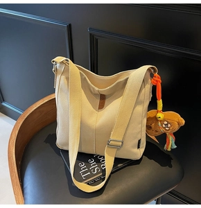 Détail du sac seau en toile avec sangle réglable et breloque ours sur une chaise