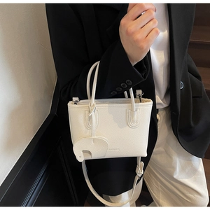 Close-up of white litchi pattern leather handbag with cute elephant charm on strap