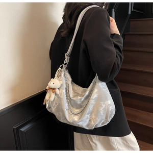 Detail of silver metallic hobo bag with chunky chain and plush bear charm on shoulder