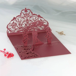 Macro view of burgundy laser-cut pop-up wedding invitation with couple in floral arch