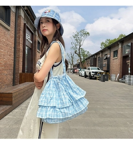 Outdoor model shot showing a light blue checkered ruffled shoulder bag and matching sun hat