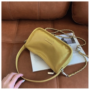 Detail of yellow leather crossbody bag with metal chain strap and logo on leather sofa