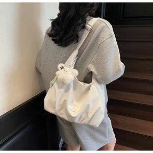 Detail of white canvas shoulder bag featuring a plush bear pendant and mesh texture