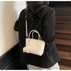 Detail of off-white lychee leather handbag with cute elephant charm and adjustable strap