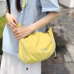 Detail of yellow nylon crossbody bag with blue drawstring and embroidered logo on front