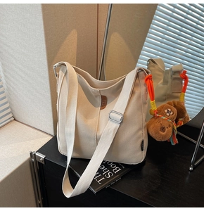 Détail d'un sac seau en toile beige avec logo en cuir et pendentif chien en peluche