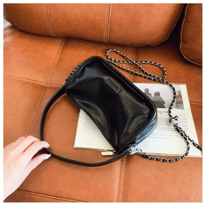 Detail of glossy black leather handbag with silver chain strap and embossed logo