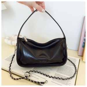 Detail of black glossy handbag with silver chain strap and hollow decorative metal ball