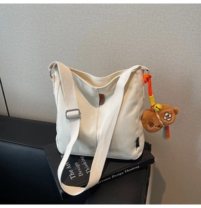 Détail du sac seau en toile blanc cassé avec breloque ours brun et large bandoulière