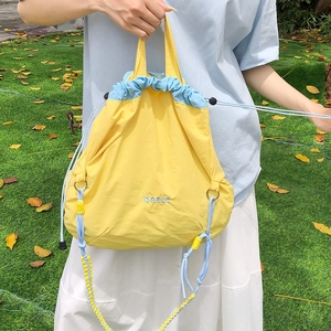 Detail of yellow nylon drawstring bag with blue straps and beaut embroidery on grass