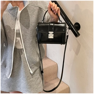 Detail of glossy black crossbody bag showing silver metal lock and textured leather