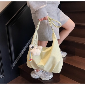 Detail of light green checkered canvas shoulder bag with a cute plush bear pendant accessory