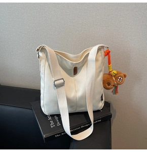 Détail du sac seau en toile avec bandoulière large et charm d'ours en peluche marron