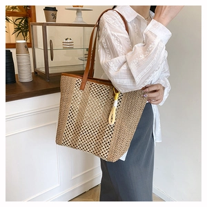 Detail of woven straw tote bag with brown leather straps and yellow tassel on shoulder