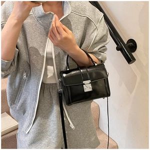 Macro view of black glossy mini flap bag with silver clasp and slim shoulder strap