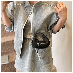 Detail of black crescent leather bag with silver chain strap on a model wearing grey outfit