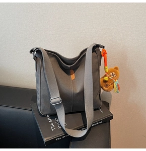 Détail du sac seau en toile grise avec logo en cuir marron et charm ours en peluche