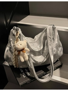 Silver metallic hobo shoulder bag with chain detail and plush bear charm on books