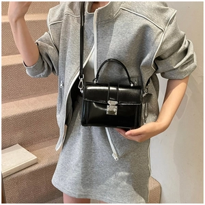 Detail of a shiny black leather crossbody bag with a silver metal clasp and top handle