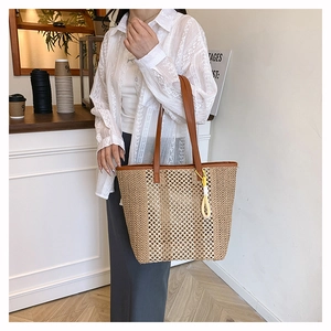 Detail of woven straw tote bag with brown leather handles and decorative tassel