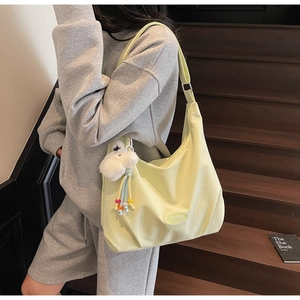 Close-up of a light yellow canvas shoulder bag featuring a white plush keychain and beads