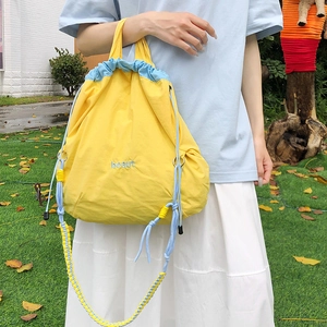 Outdoor shot of a yellow nylon drawstring crossbody bag with light blue straps and handles