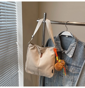 Détail du sac seau en toile beige avec écusson en cuir et breloque ours brun mignonne