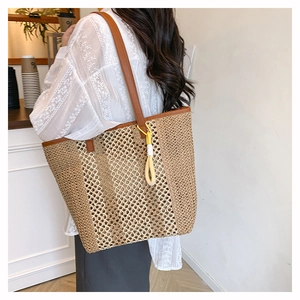 Detail of a large woven straw tote bag with brown leather straps and colorful rope tassel