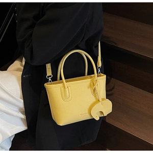 Close-up of yellow lychee textured leather tote with elephant charm on dark background