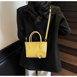 Detail of yellow lychee pattern handbag with a cute elephant charm on a model