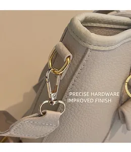 Detailed close-up of golden metal swivel hook and D-ring on beige lychee leather bag