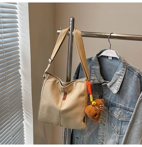 Détail d'un sac seau en toile beige avec étiquette en cuir et breloque ours en peluche